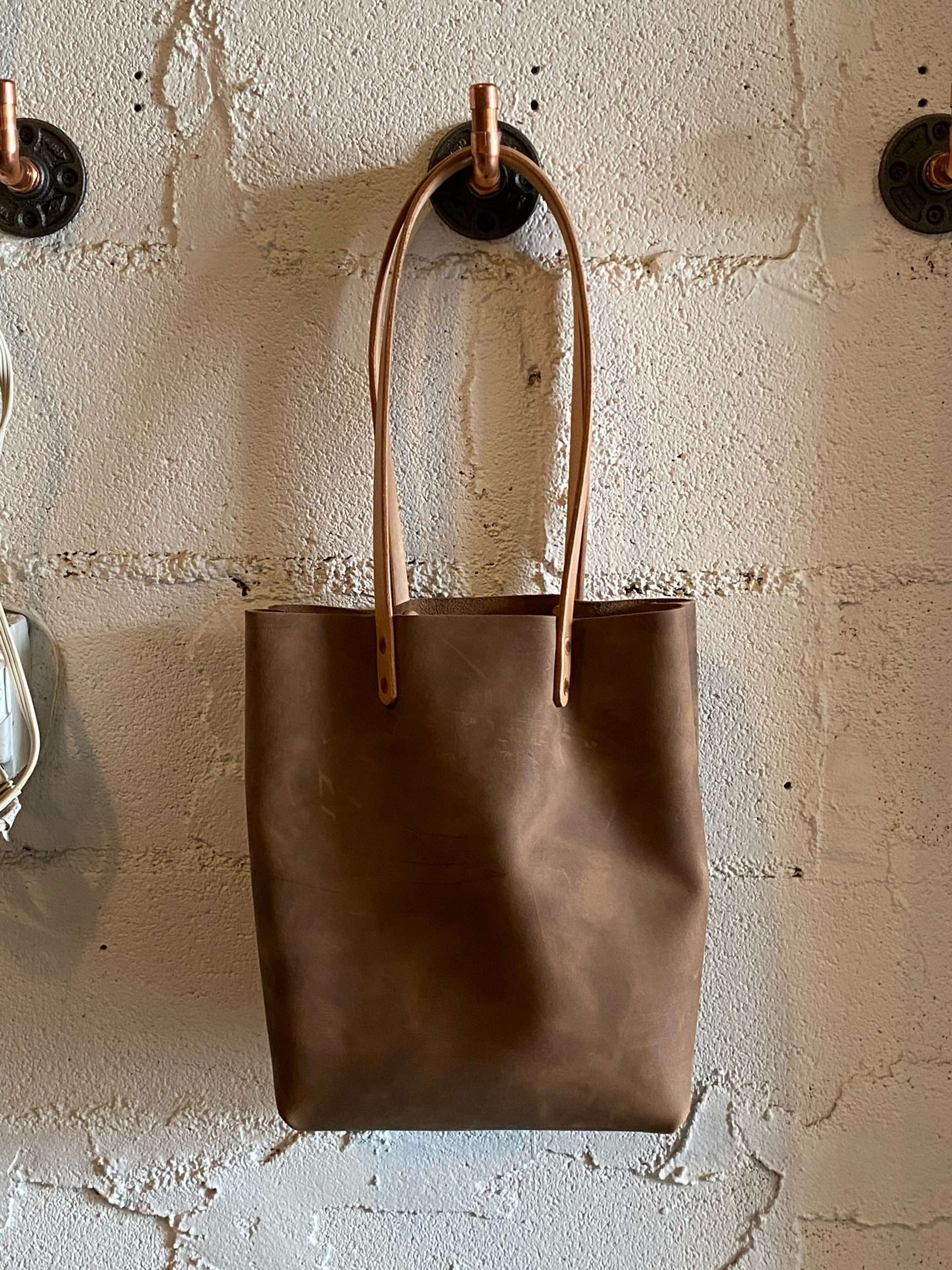 Leather tote bag on metal hook against white brick wall
