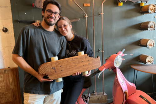 a couple holds up a wooden longboard they made together during a unique date night idea in brooklyn