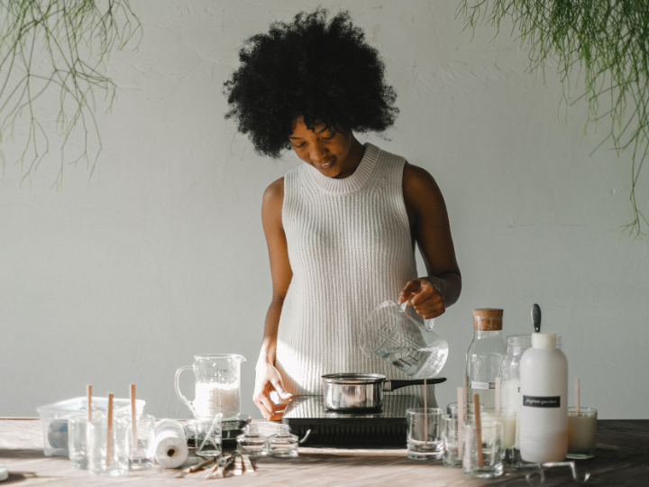 A woman in a white tank top makes candles at a wooden table