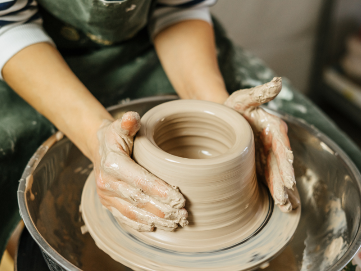 A person's hands are shown working wet clay on a pottery wheel