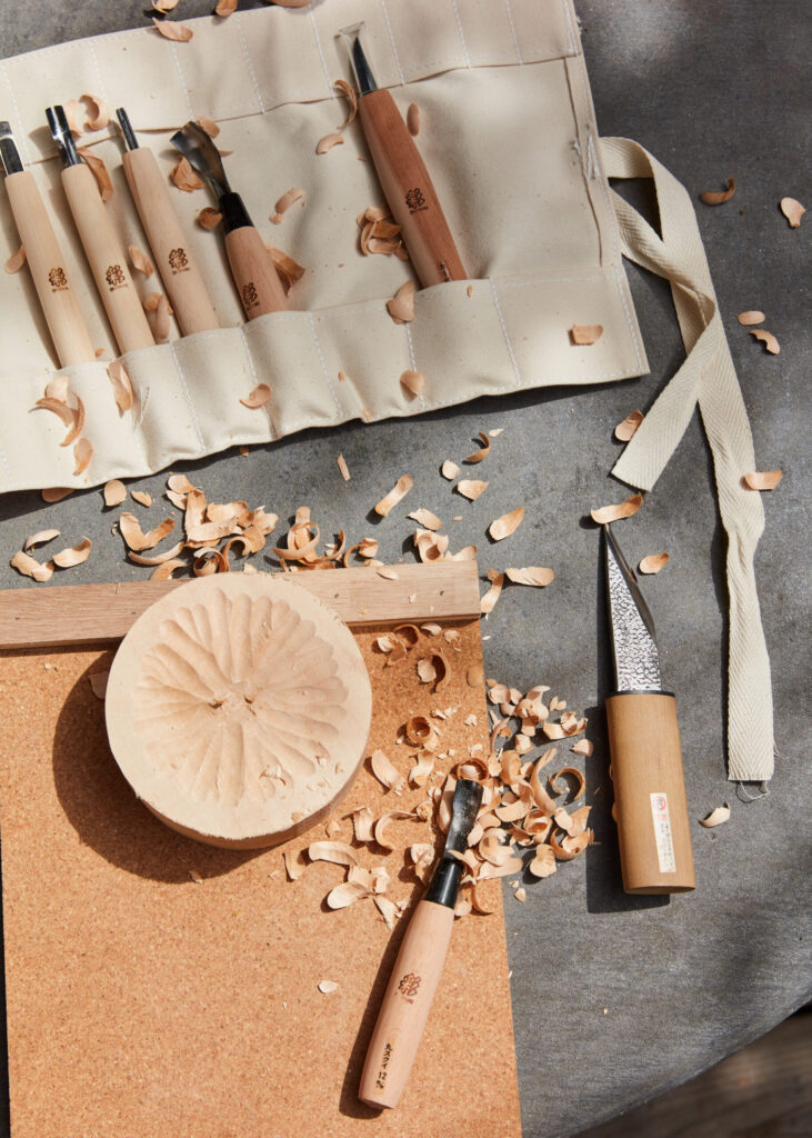 Tools, shavings, and a part of a wooden bowl laying on a table.
