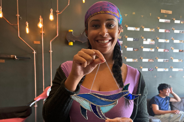 A woman holds up her stained glass creation made at Craftsman Ave