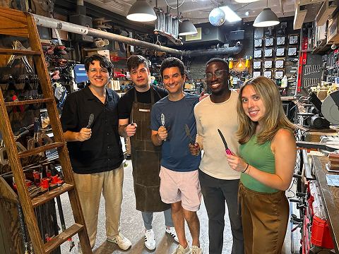 a large group in nyc smiles as they hold up their homemade knives from a craftsman ave workshop